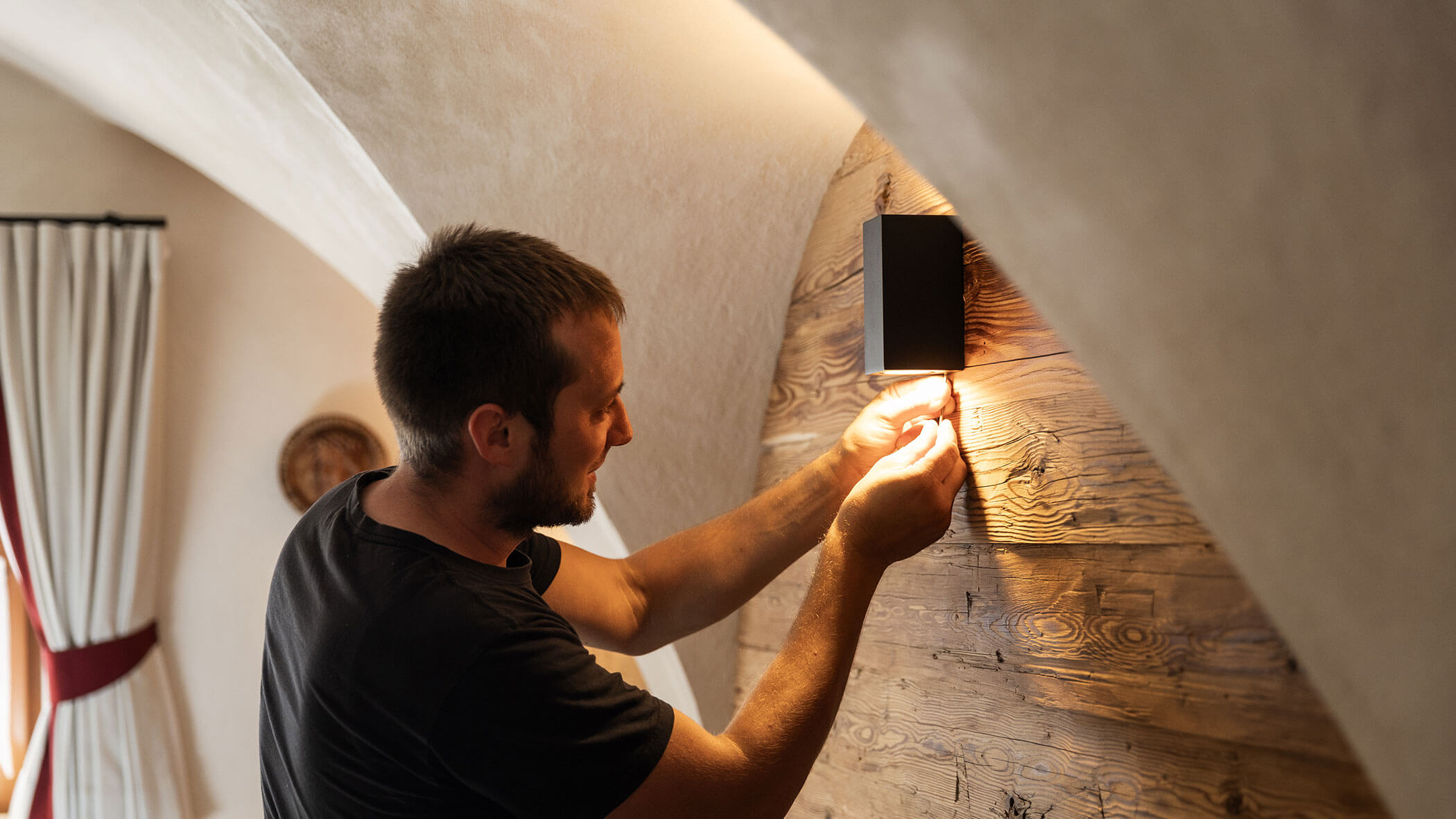 Elektriker montiert eine Lampe an eine Holzwand - Elektro Felderer